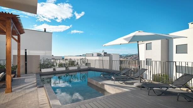 A rooftop pool with lounge chairs and umbrellas, surrounded by a wooden deck and a white building. - Luxury Villa Natali w Pool, Terrace and sea View (Podstrana)
