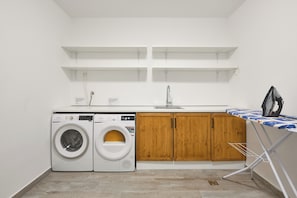 Ein Waschraum mit Waschmaschine, Trockner, Holzausbau, einem Waschbecken und einem Bügelbrett.