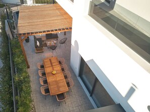 Eine Außenpatio mit Holztisch und Stühlen, eine kleine Sitzecke mit Sofa und Couchtisch, und Blick auf die Fassade des Gebäudes.