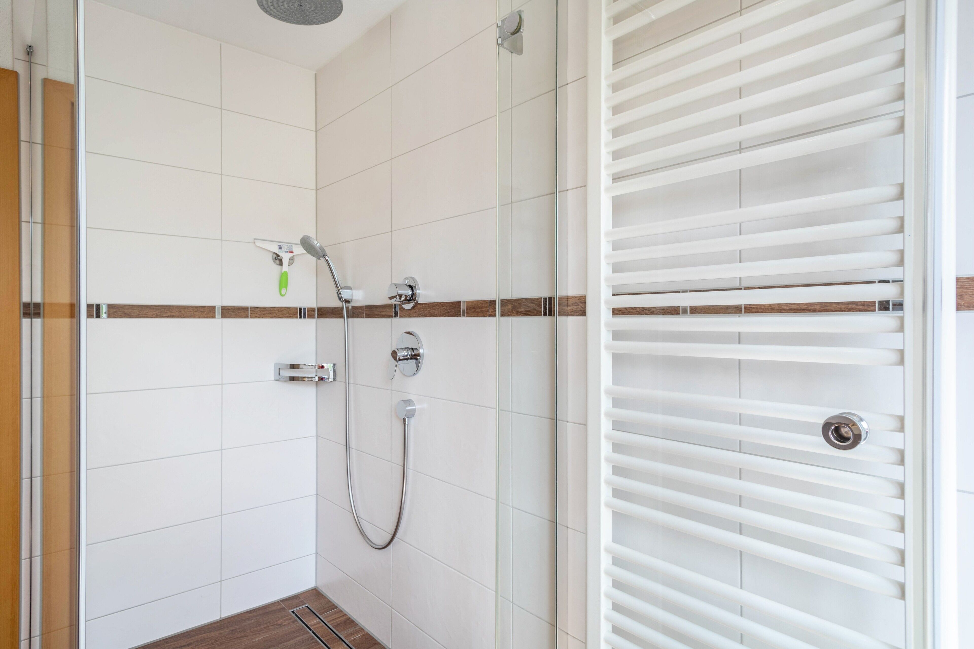 Ein modernes Badezimmer mit weißen Fliesen, einer Glasdusche und einem weißen Handtuchhalter.