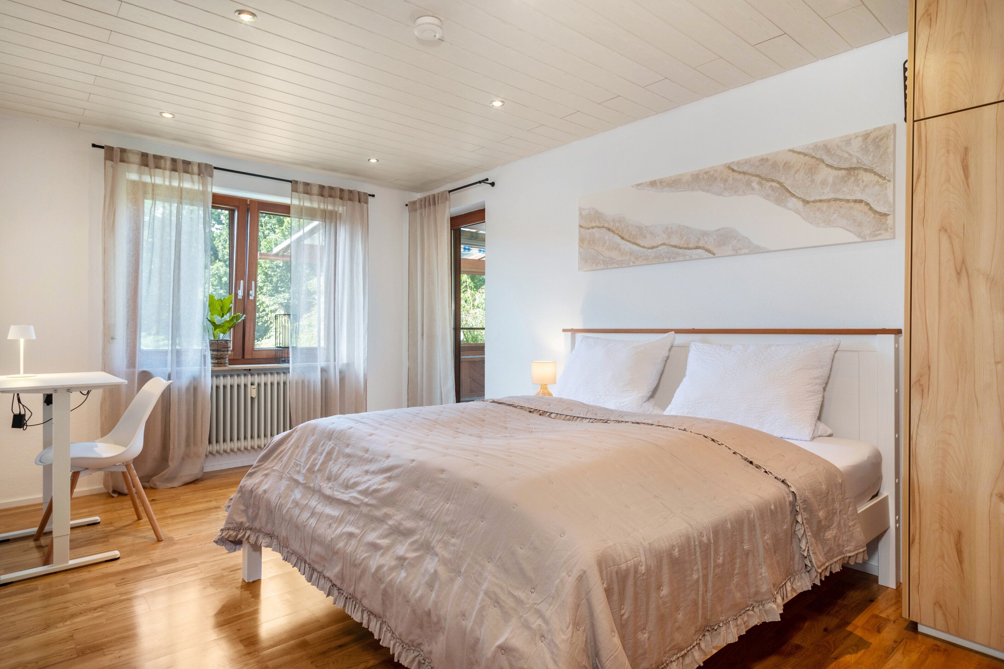Ein Schlafzimmer mit Bett, Schreibtisch, Stuhl, Heizkörper und einem Fenster mit Vorhängen.