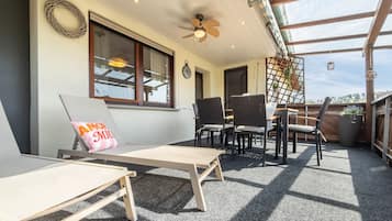 Une terrasse ensoleillée avec deux chaises longues, une table et un ventilateur de plafond.