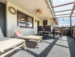 Eine sonnendurchflutete Terrasse mit zwei Liegestühlen, einem Tisch und einem Deckenventilator.