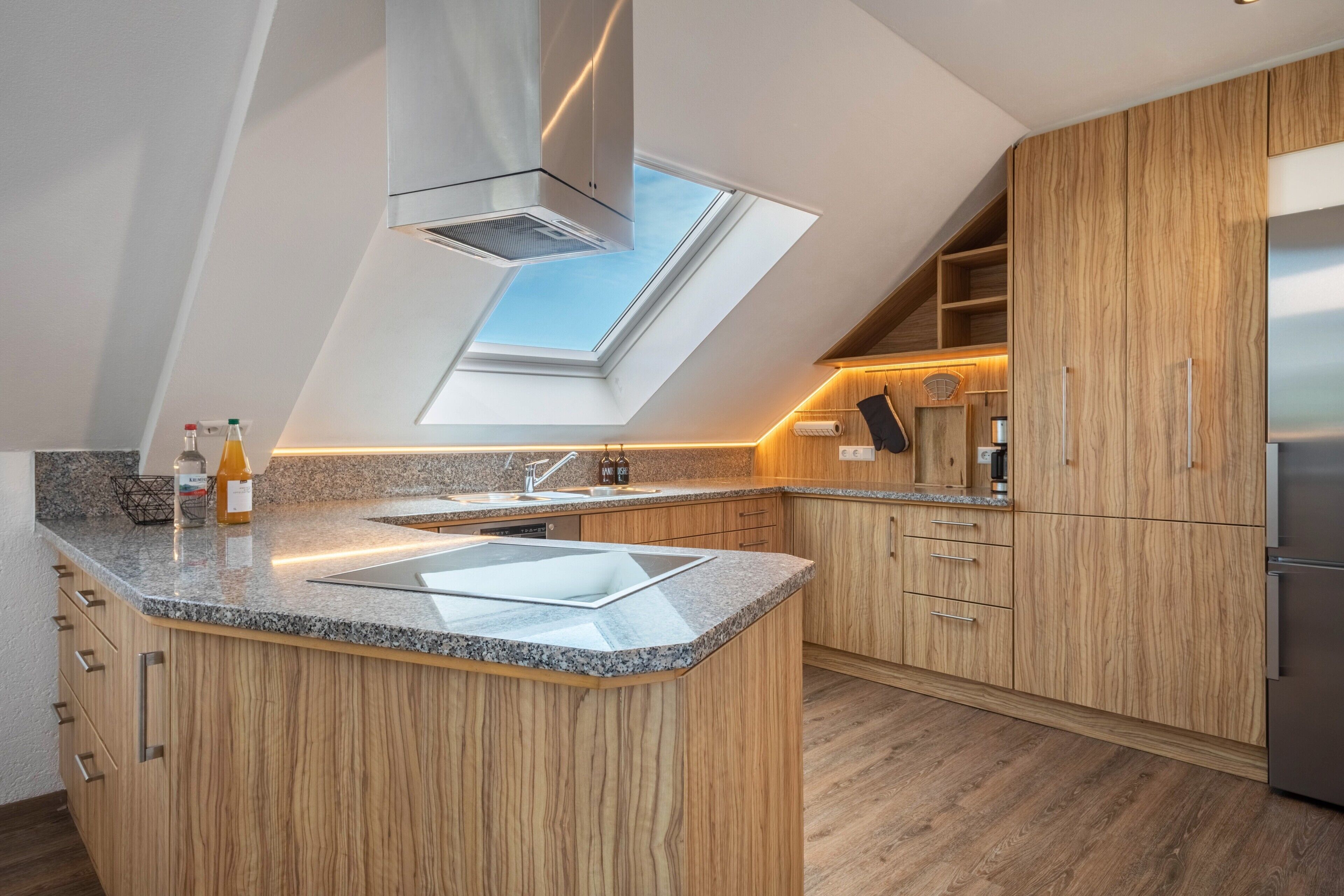 A modern kitchen with a skylight, granite countertops, wooden cabinets, and a stainless steel refrigerator.