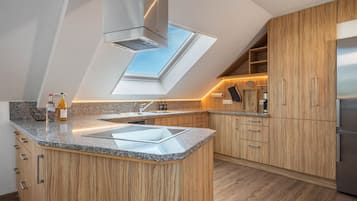 A modern kitchen with a skylight, granite countertops, wooden cabinets, and a stainless steel refrigerator.