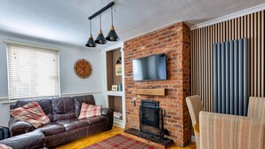 A living room with a brick fireplace, leather sofa, and a flat-screen TV mounted on the wall. - Ty Pen Y Bryn, Castle Views (Conwy)