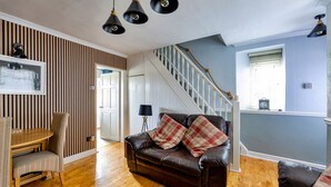A living room with a brown leather sofa, a wooden dining table, and a striped wall. - Ty Pen Y Bryn, Castle Views (Conwy)