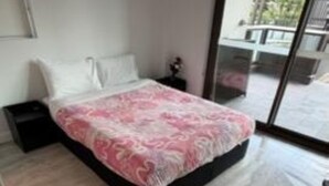A modern bedroom with a large bed, a nightstand, a dresser, and a sliding glass door leading to an outdoor area.