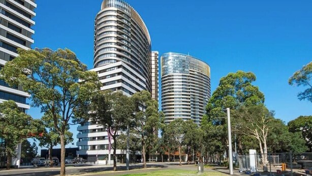 A modern urban area with high-rise buildings, a grassy area, and trees.