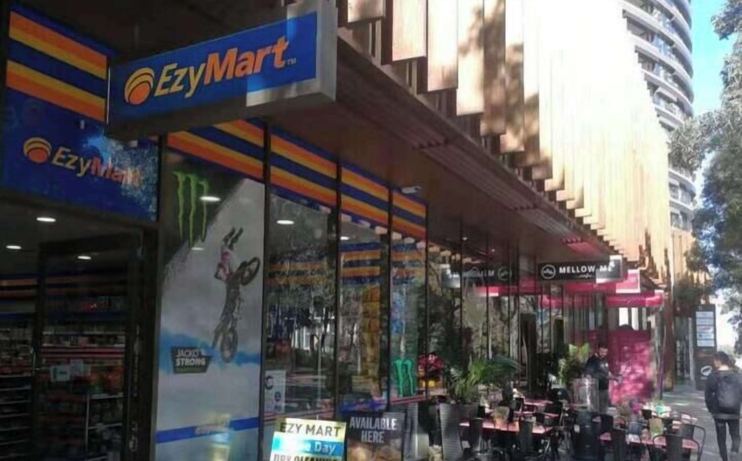 A storefront with a clear sign for EzyMart, a store with a visible motorcycle advertisement, and a visible storefront for Mellow.
