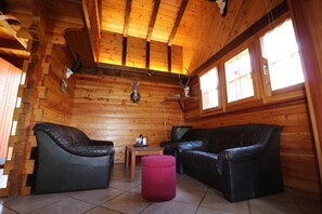 A wooden cabin interior with two leather sofas, a red ottoman, and deer antlers on the walls. - Chalet Nid d Aigle - 6 personnes - Farquesses (Les Haudères)
