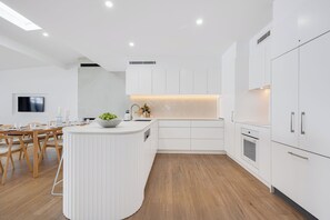 A modern kitchen with white cabinetry, a wooden dining table, and a built-in island. - Absolute Beachfront - Seaside Serenity - sand dunes - Currimundi, Sunshine Coast (Currimundi)