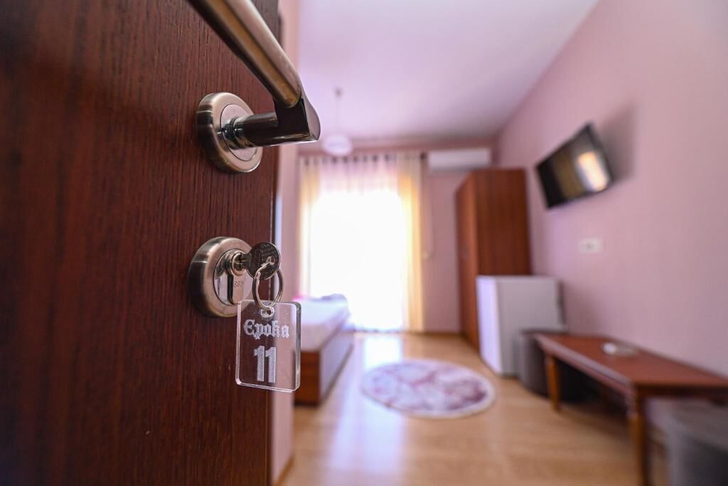 Ein Hotelzimmer mit Holztür, Schlüsselanhänger mit der Zimmernummer, einem Bett, einem Fernseher und einem kleinen Tisch.