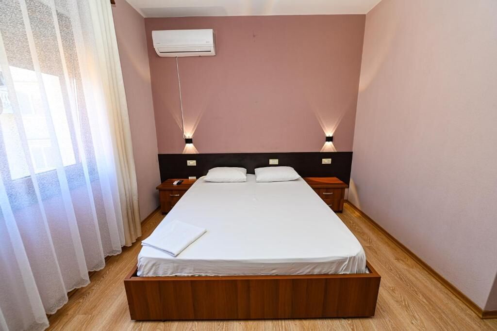 Ein Schlafzimmer mit Bett, Nachttischen, einer Klimaanlage und einem Fenster mit Vorhängen.
