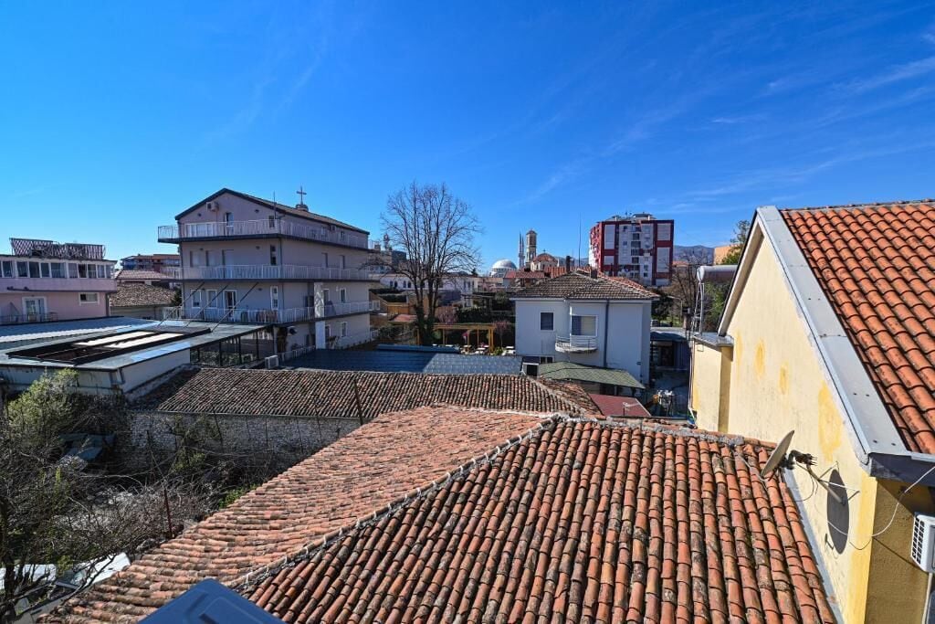 A residential area with terracotta-tiled roofs, a mix of single and multi-story buildings, and a clear blue sky.