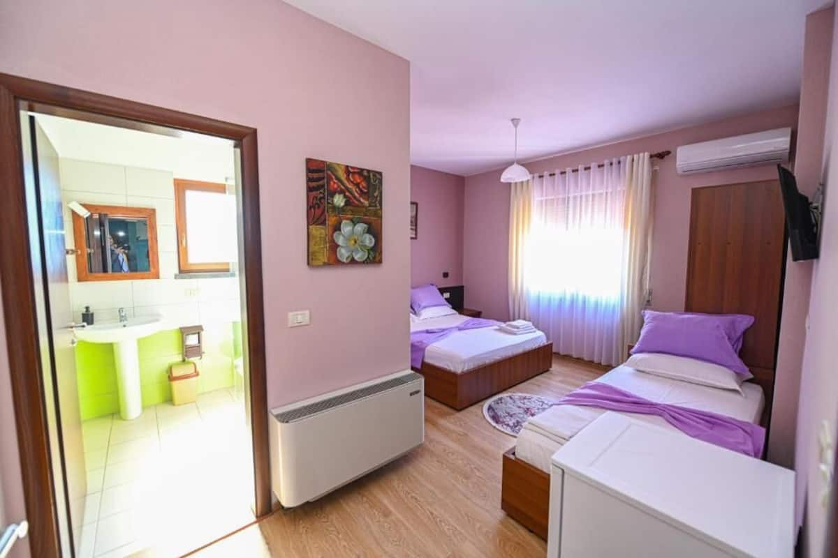 Un dormitorio con dos camas, una ventana con cortinas, un radiador y un cuadro en la pared.