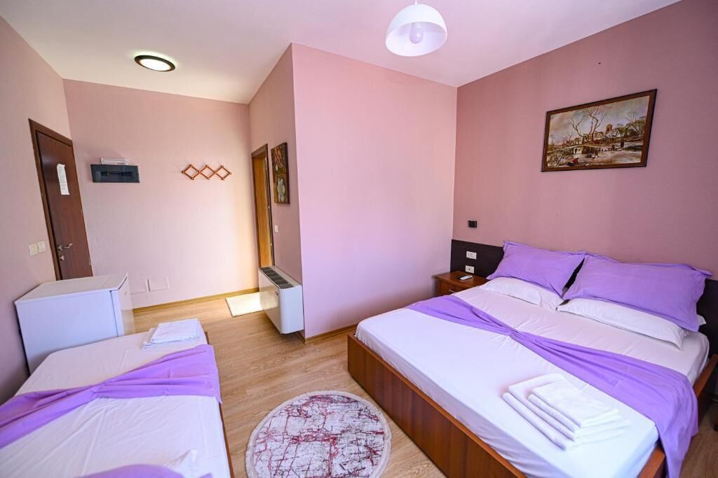 A bedroom with two beds, a heater, a small desk, and a painting on the wall.