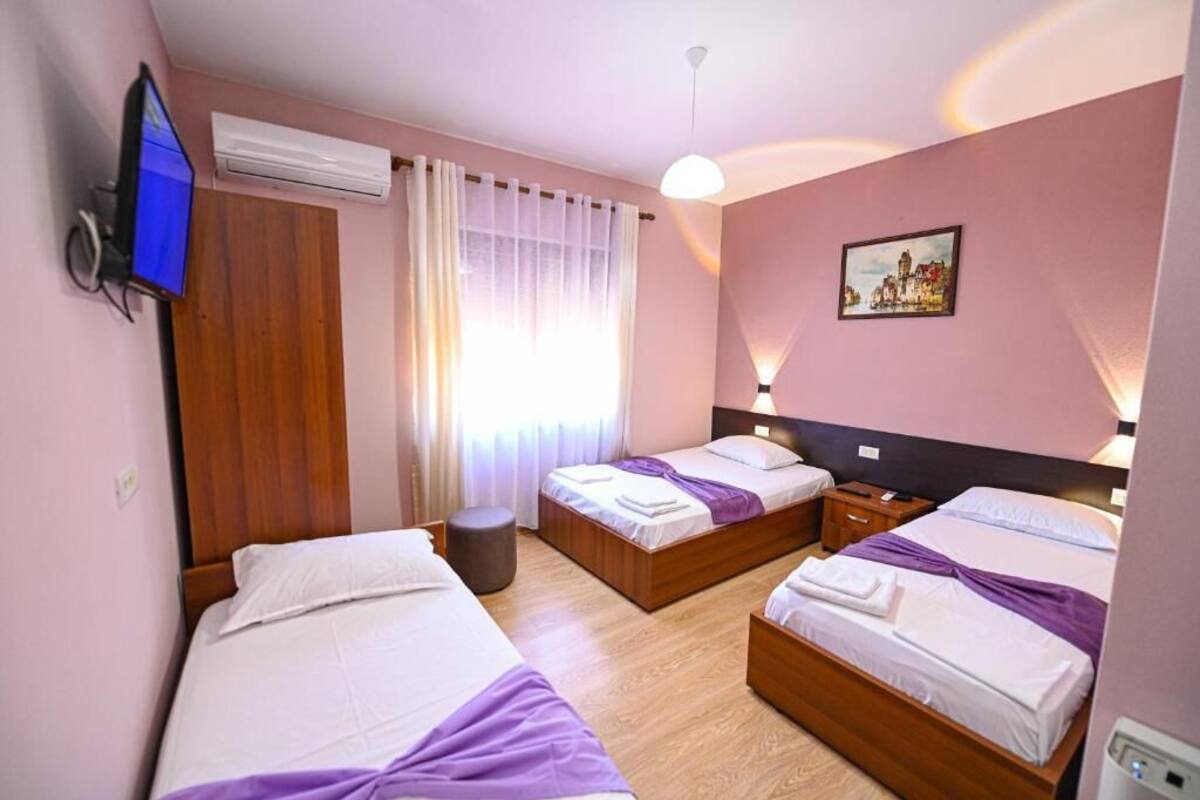 Habitación de hotel con dos camas, televisión, aire acondicionado, ventana con cortinas y un cuadro en la pared.