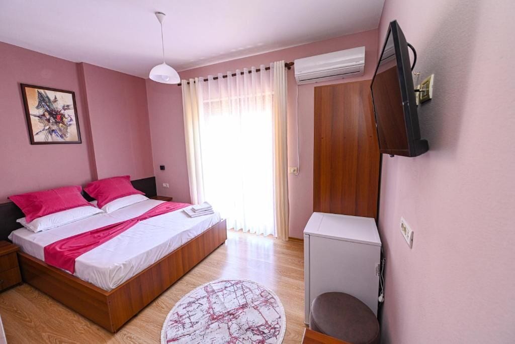 A bedroom with a bed, bedside table, TV, and an air conditioning unit.