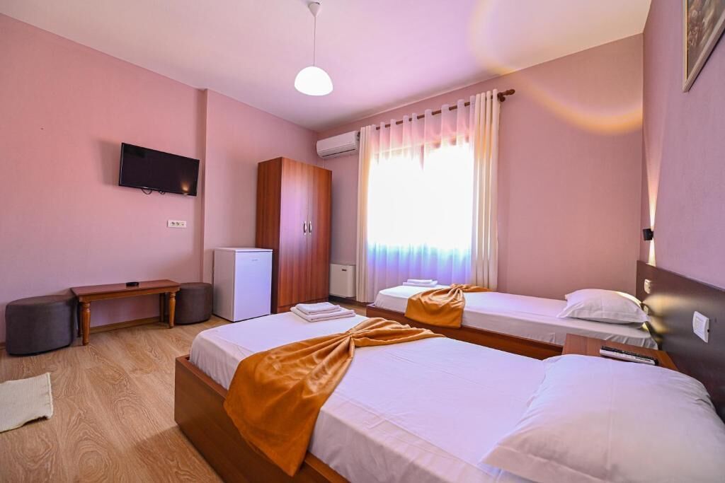 Habitación de hotel con dos camas, televisión, escritorio y ventana con cortinas.