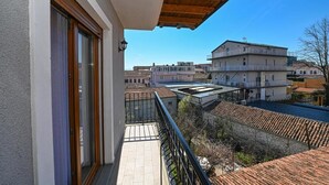 Un balcón con vista a edificios cercanos, techo de madera y puerta de cristal.