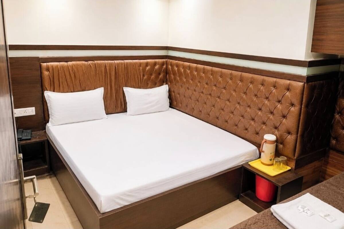 A neatly made bed with a brown headboard, a bedside table with a red container, and a small table with a yellow tray.