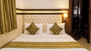 A hotel room with a tufted headboard, two pillows, a bedspread, and a nightstand with a lamp.