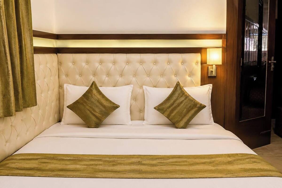 A hotel room with a tufted headboard, two pillows, a bedspread, and a nightstand with a lamp.