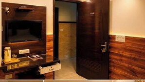 A hotel room with a wooden panel wall, a flat-screen TV, a coffee machine, and a door with a handle.