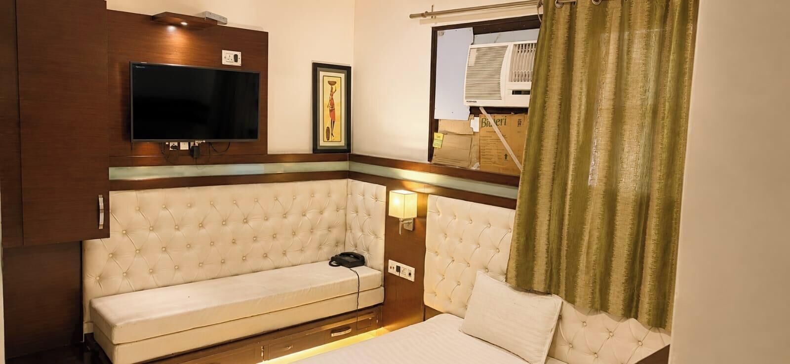 A room with a sofa, a bed, a TV mounted on the wall, and an air conditioning unit.