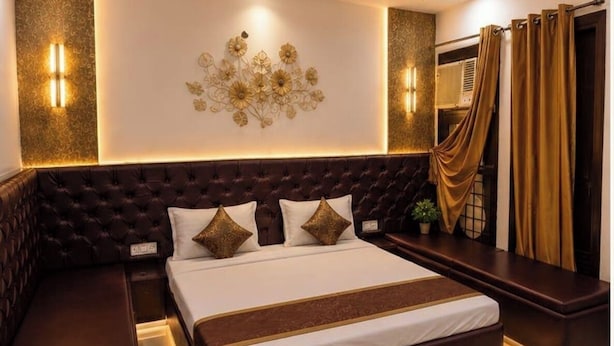 A bedroom with a large bed, a headboard, bedside tables, wall sconces, and a decorative wall piece.
