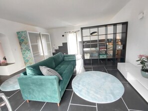 A modern living room with a teal sofa, a round coffee table, and a glass partition wall. - Charmant appartement de caractère de 90 mq dans ancienne maison en pierres (Saint-Paulet-de-Caisson)