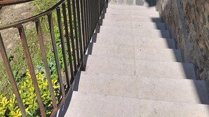Una escalera de piedra que conduce a un arco de piedra, rodeado de vegetación y una barandilla de metal.
