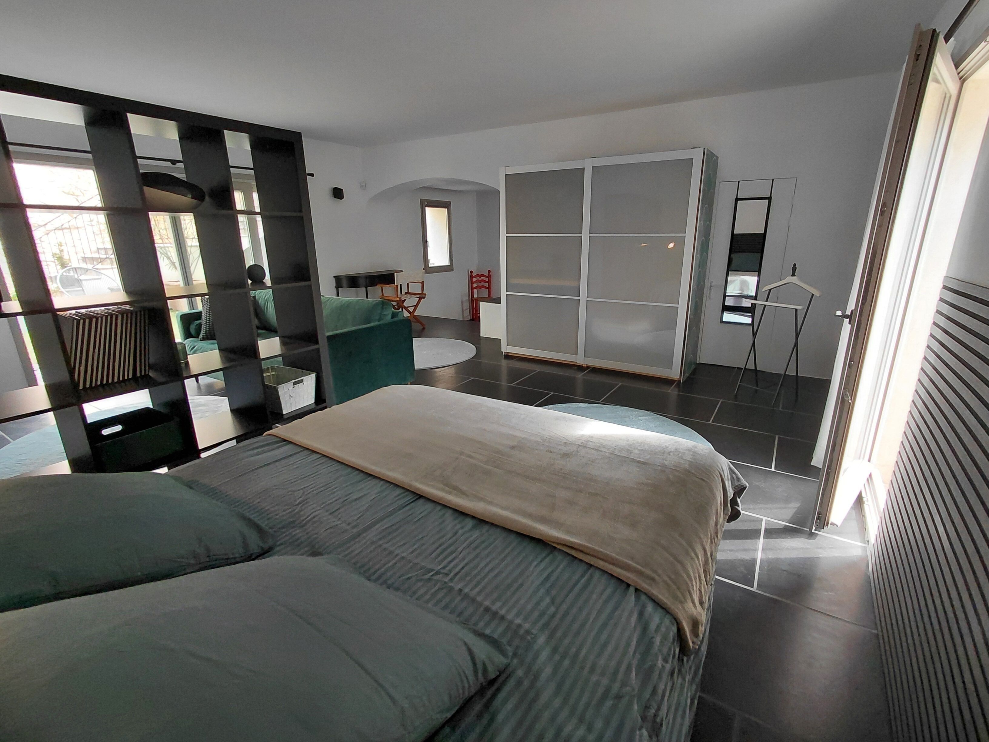 Une chambre moderne avec un grand lit, un fauteuil vert, une armoire et un miroir.
