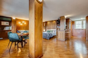 A spacious room with a wooden floor, a dining area with chairs, a bed with pillows, and built-in wooden shelves. - BDC - The Roman Cottage! Free parking! (Rome)