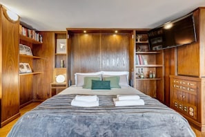 A hotel room with a large bed, wooden paneling, a flat-screen TV, and built-in bookshelves. - BDC - The Roman Cottage! Free parking! (Rome)