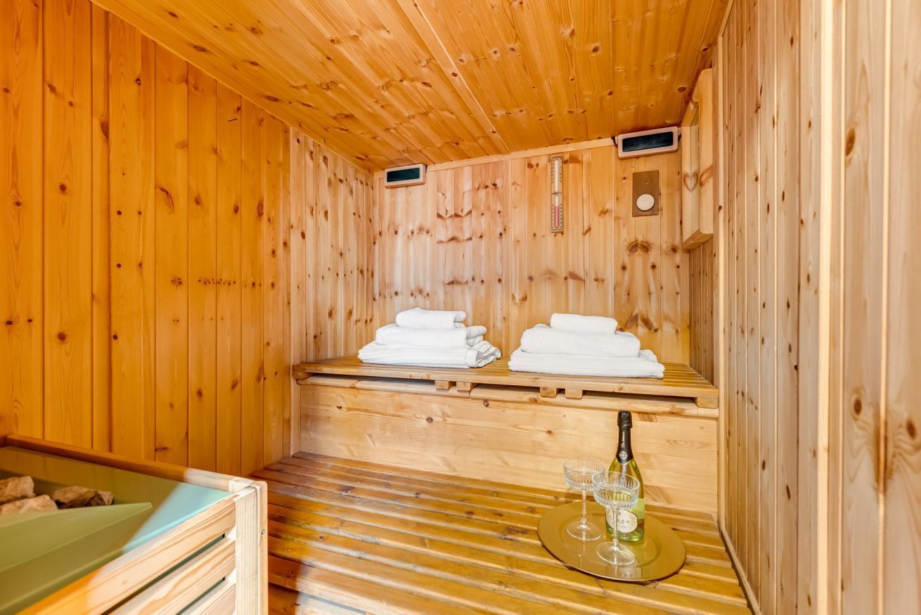A wooden sauna room with benches, towels, a bottle, and glasses.
