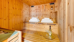 Un sauna de madera con bancos, toallas, una botella y vasos.