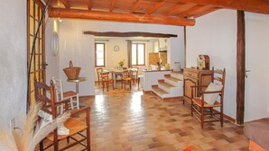 Amplia sala de estar con piso de madera, una mesa de comedor, sillas y un área de cocina con un armario de madera y un reloj.