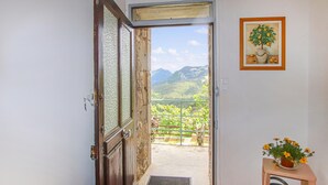 Una puerta abierta que da a un balcón con vistas a la montaña, un cuadro enmarcado en la pared y una pequeña mesa con una planta en maceta.