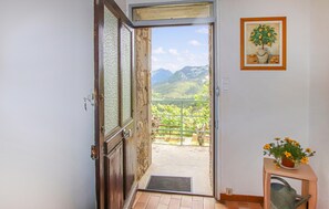 Eine geöffnete Tür, die auf einen Balkon mit Bergblick führt, ein gerahmtes Bild an der Wand und ein kleiner Tisch mit einem Blumentopf.