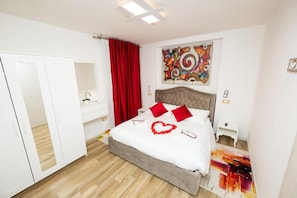 A bedroom with a bed, a dresser, a vanity, a red curtain, a colorful abstract painting, and a heart-shaped decoration on the bed. - Isa Sweet Home (Venezia)