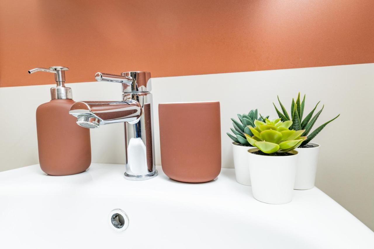 Une salle de bain avec un robinet moderne, une tasse marron et deux plantes en pot.