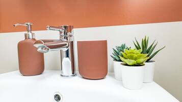 Une salle de bain avec un robinet moderne, une tasse marron et deux plantes en pot.