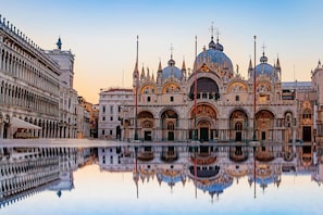 Un bâtiment historique à l’architecture riche et ornée, doté d’un dôme central et dont l’image se reflète dans l’eau.
