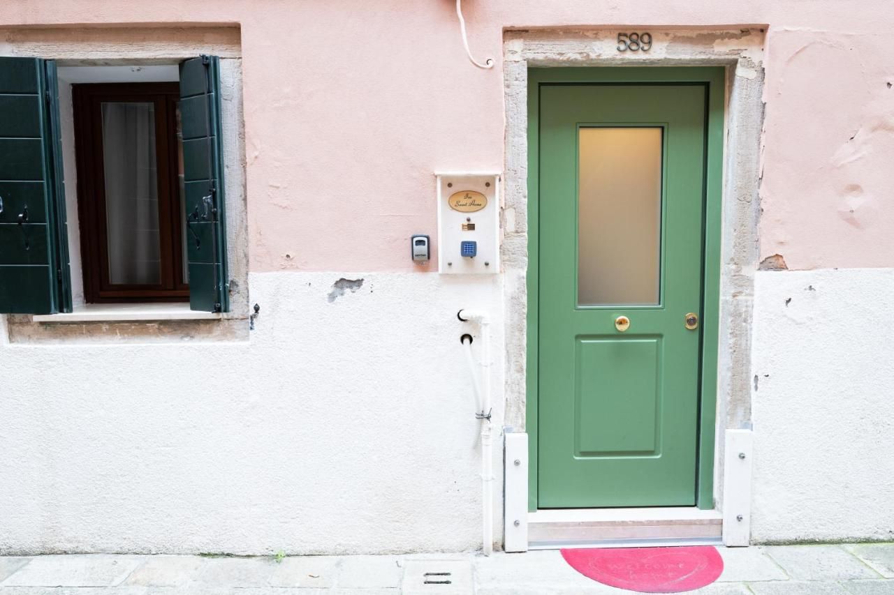 Eine grüne Tür mit Schild, ein Fenster mit Rollläden und ein kleines Stromdosenfach an der Wand.