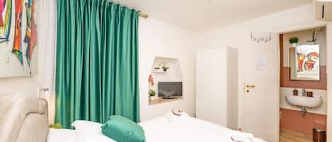 A hotel room with a bed, a TV, a bathroom with a sink, and a door leading to another room.