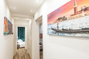 Un couloir orné d’un tableau représentant un paysage urbain, un lit avec des rideaux turquoise et un plancher en bois.