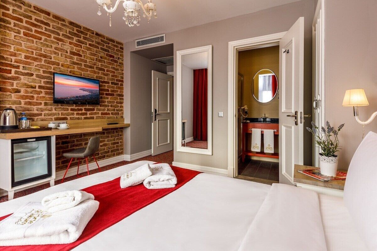 Habitación de hotel con pared de ladrillo, televisor, escritorio, cama, baño y candelabro.