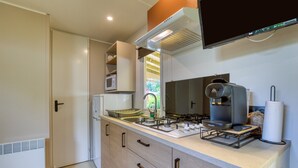 A modern kitchen with a gas stove, a coffee maker, and a built-in oven. - Bungalow with Private Pool, Private Terrace, and Air Conditioning (Agde)